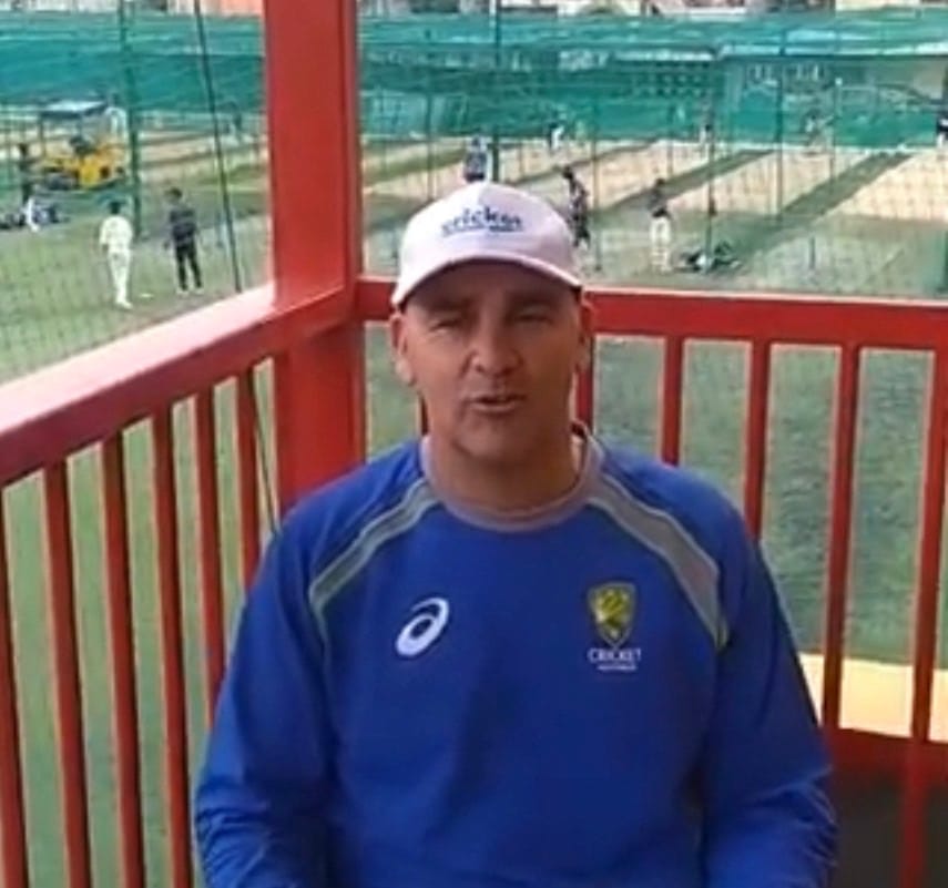 Andrew Walton speaking from a balcony above a row of practice nets where players are training.